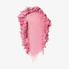 Blush-Puder in der Farbe petite, als kräftiger Farbstrich mit krümeligen, unregelmäßigen Rändern auf weißem Hintergrund.