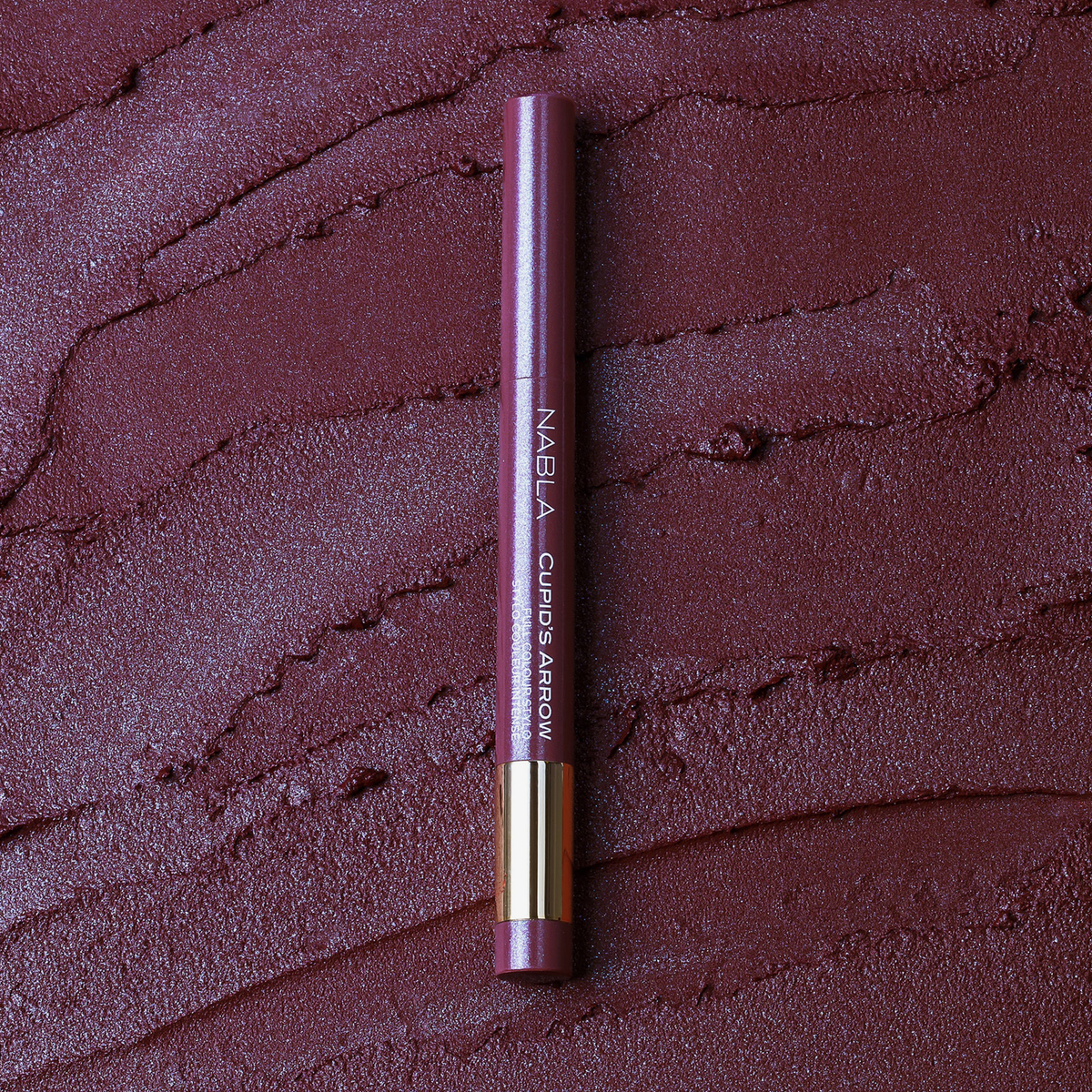 NABLA Cupid’s Arrow Longwear Stylo Arrow Shine in der Nuance Bewitched auf strukturierter, bordeauxfarbener Oberfläche.