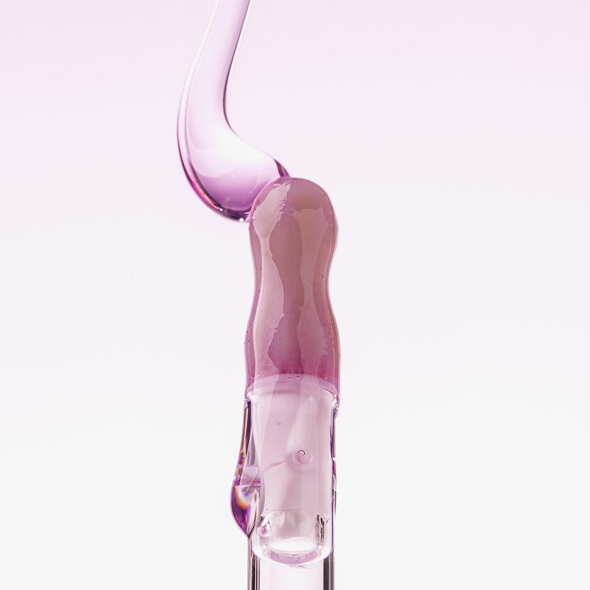 Ein Tropfen Lip Candy Oil in Lila gleitet vor einem hellrosa Hintergrund über den Applikator. 