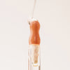 Ein Tropfen Lip Candy Oil in der Farbe Honey gleitet vor einem pfirsichfarbenem Hintergrund über den Applikator.
