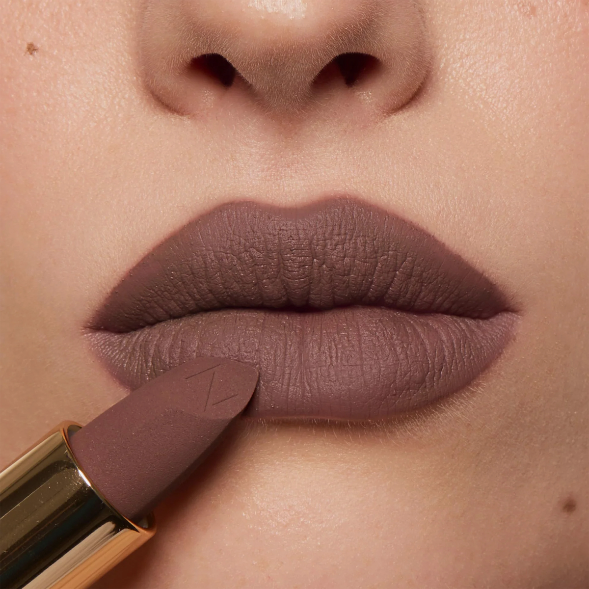 Nahaufnahme von Lippen mit dem Nabla Cosmetics Matte Pleasure Lipstick in der Farbe Taupe Talk, während der Lippenstift direkt auf die Unterlippe aufgetragen wird.