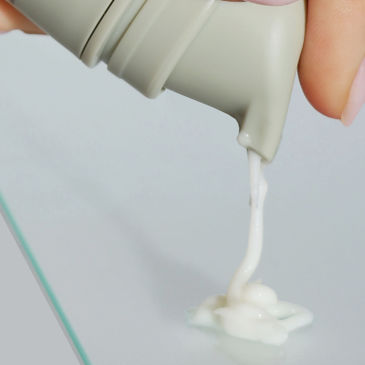 Eine Hand drückt das NERDS. 10% Azelainsäure Cremeserum aus einer grauen Tube auf eine klare Glasfläche.