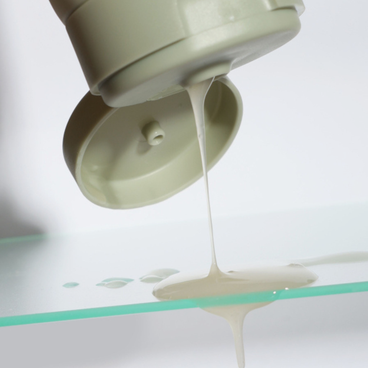 Beige NERDS-Cleanser wird aus geöffneter Flip-Top-Tube auf eine Glasplatte gegossen.