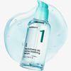 Eine klare Flasche numbuzin No.1 Pantothenic B5 Active Soothing Serum mit einer türkisfarbenen Pumpe befindet sich auf einem gelartigen Hintergrund.