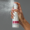 Vor einem grauen Hintergrund sprüht eine Hand den Leave-in-Conditioner „Daily Damage Defence“ von Philip Kingsley auf.