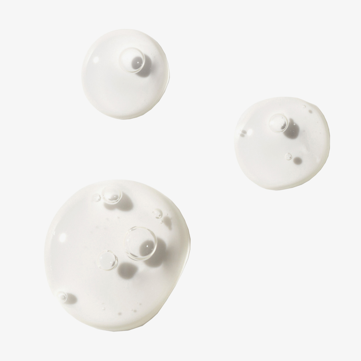 Drei klare, runde Serumtröpfchen des „Philip Kingsley Overnight Scalp Barrier Serum“ mit Bläschen im Inneren vor einem weißen Hintergrund.
