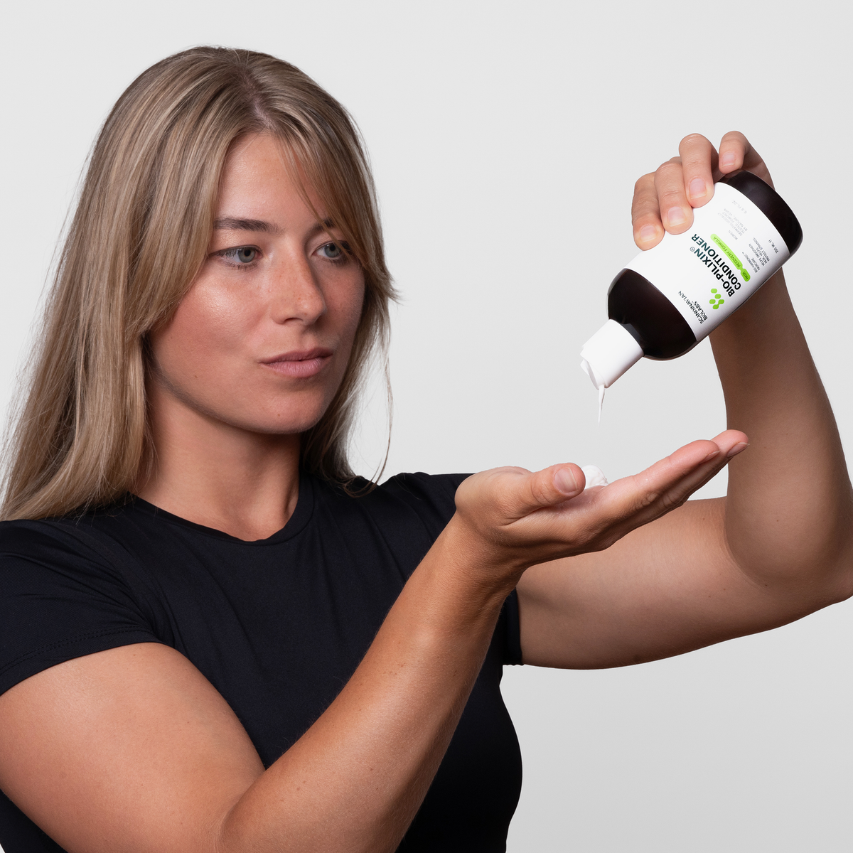 Eine Frau gibt Bio-Pilixin® Conditioner+ Women von Scandinavian Biolabs vor einem schlichten weißen Hintergrund in ihre Hand.