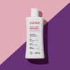 Weiße Flasche Root Cause Hair Retreat Shampoo auf rosa Hintergrund mit einem violetten diagonalen Streifen, der einen Schatten wirft.