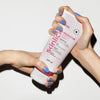 Zwei Hände mit blauem Nagellack halten eine Tube Rouge365 Essential Cream vor einem weißen Hintergrund.