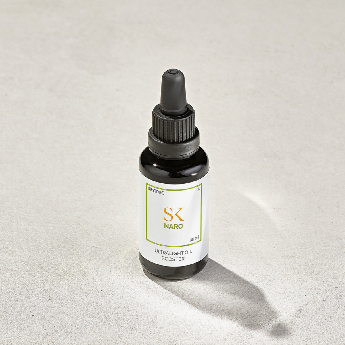 Auf einer hellgrauen Oberfläche steht eine schwarze Tropfflasche mit der Aufschrift „Naro Ultralight Oil Booster“.