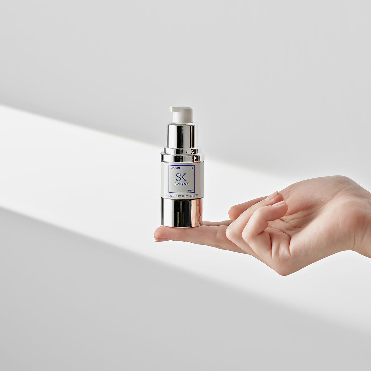 Eine Person balanciert eine Flasche Sphynx-Serum auf ihren Fingerspitze vor einem minimalistischen weißen Hintergrund.