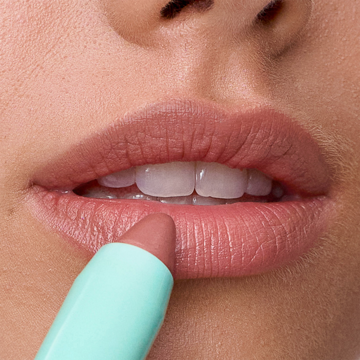 In einer Nahaufnahme trägt eine Person den Lippenstift „SWEED Le Lipstick“ in der Farbe Nude-Pink aus einer mintgrünen Tube auf ihre Lippen auf.
