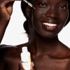 Eine Frau trägt mit einer Pipette Hautpflegeserum auf ihr Gesicht und hält eine weiße Flasche mit der Aufschrift „Argan Oil 100 % Pure“ in der Hand.