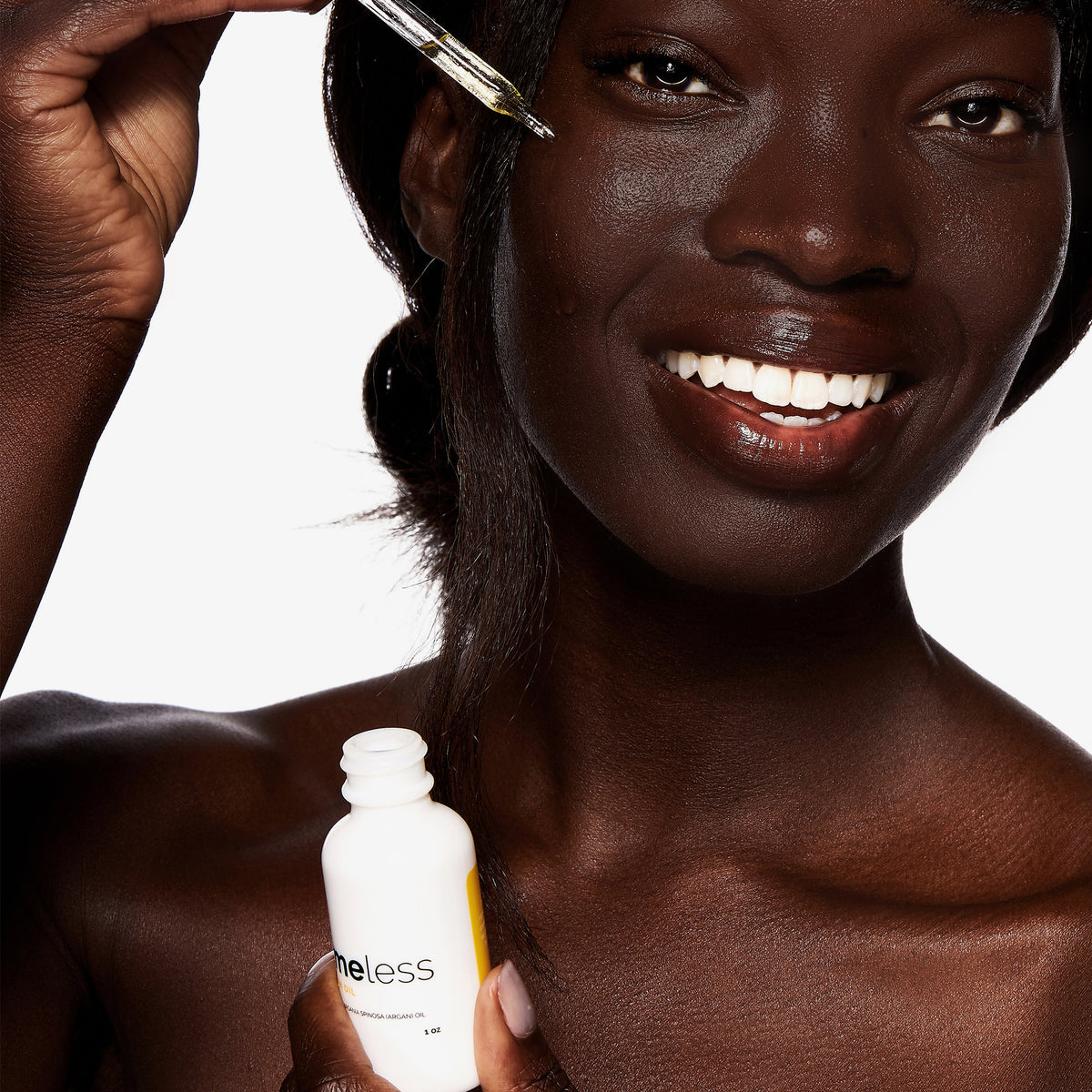 Eine Frau trägt mit einer Pipette Hautpflegeserum auf ihr Gesicht und hält eine weiße Flasche mit der Aufschrift „Argan Oil 100 % Pure“ in der Hand.
