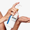 Hände geben vor einem schlichten Hintergrund 100 % reines Hyaluronsäure-Serum aus einer Pumpflasche in eine offene Handfläche.