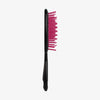 Die UNbrush Detangling Hair Brush hat rosa Borsten und einen schwarzen Griff, der aufrecht vor einem schlichten weißen Hintergrund steht.