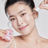 Eine Frau trägt mit einer Pipette Serum auf ihr Gesicht auf und hält eine rosa Flasche mit der Aufschrift „Peach 70 % Niacinamide Serum“ in der Hand.