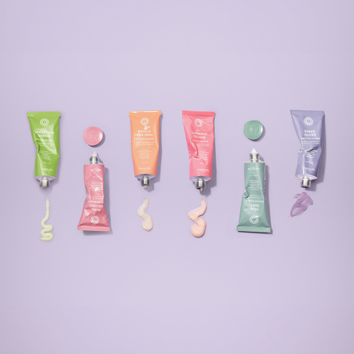 Sechs bunte Tuben Booster Masque von maria nila, jeweils mit passenden Kappen und Produktswatches auf einem lavendelfarbenen Hintergrund.