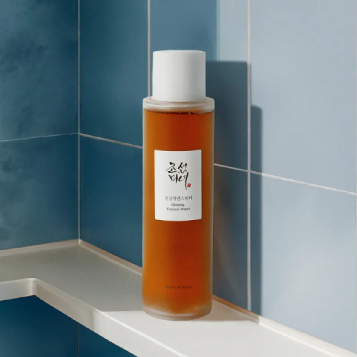 In einem blau-gefliesten Badezimmerregal steht das Ginseng Essence Water von Beauty of Joseon