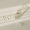 Offene Tube Relief Sun: Rice + Probiotics liegt auf einer hellen Oberfläche, daneben wirft ein cremefarbener Swatch der Lotion