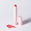 Ein rosafarbener „BLONDESISTER 2 IN 1 IT’S UP TO YOU LIP OR CHEEK“-Stift liegt neben seiner Kappe, auf der ein korallenfarbener Farbmuster auf weißem Hintergrund zu sehen ist.