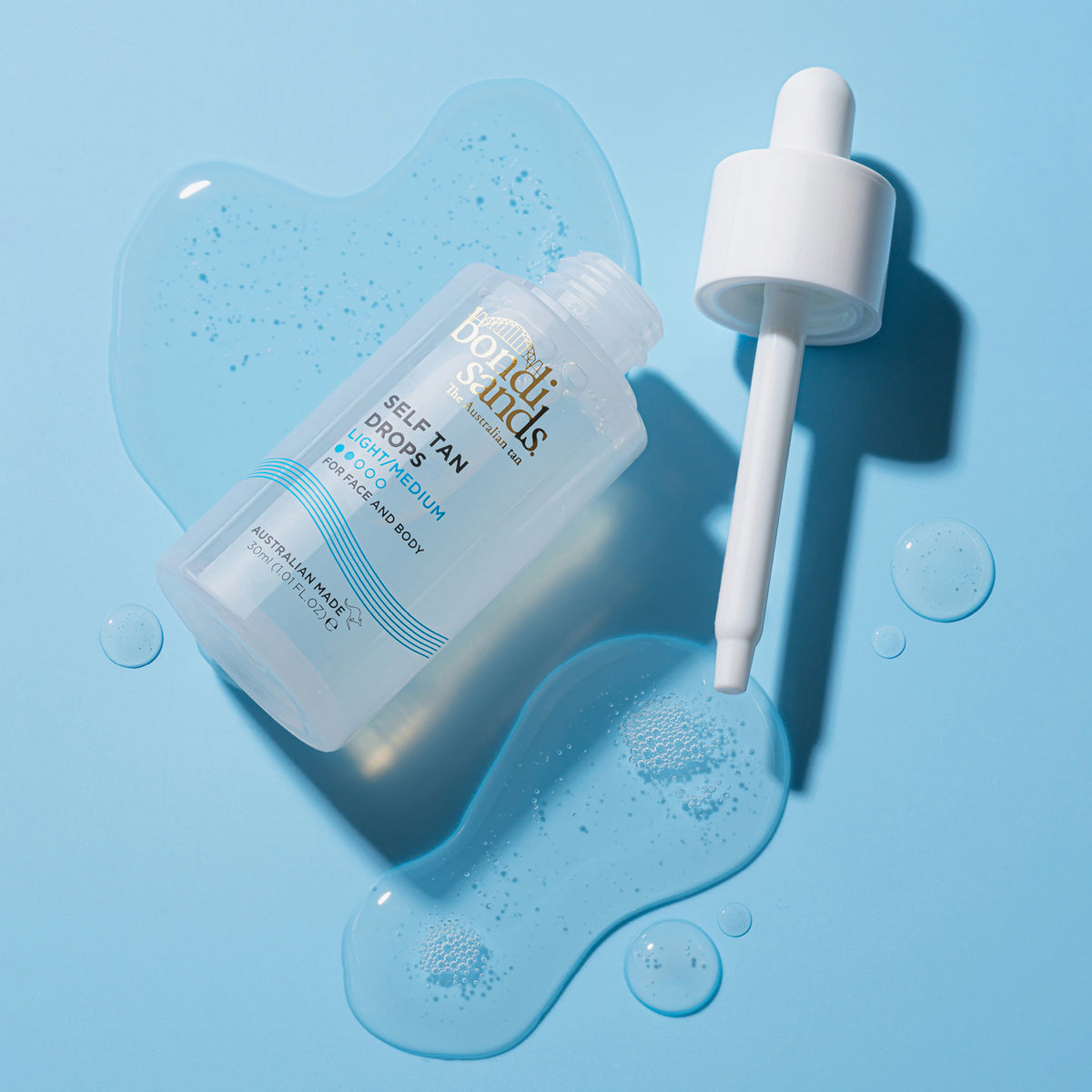Eine geöffnete und ausgelaufene Flasche Self Tan Drops Light/ Medium liegt auf einer blauen Oberfläche