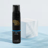 Eine schwarze Flasche Self Tanning Foam Dark von Bondi Sands neben einem weißen Würfel auf blauer Oberfläche