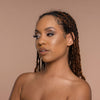 Person mit geflochtenem Haar und neutralem Make-up zeigt den Cronzer Cream Bronzer Acron vor beigem Hintergrund.