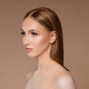 Eine Frau mit glattem braunem Haar und dezentem Make-up, aufgepeppt mit Cronzer – Cream Bronzer, blickt vor einem beigen Hintergrund zur Seite.