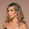 Eine Frau mit lockigem blondem Haar blickt vor einem neutralen Hintergrund zur Seite und präsentiert den Cronzer - Cream Bronzer.