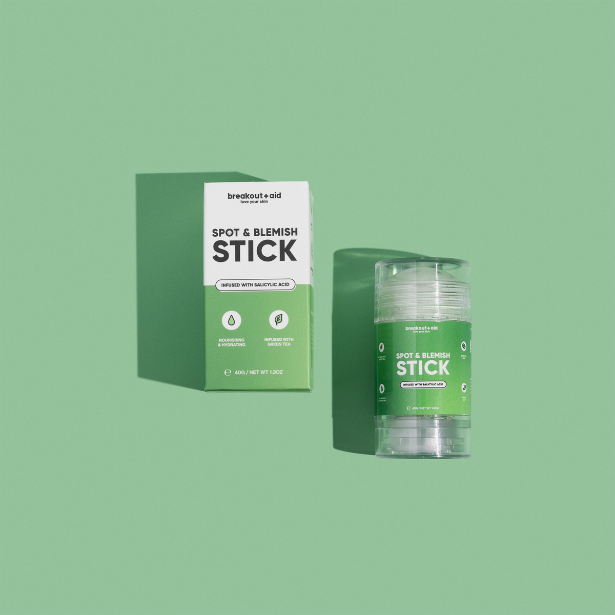 Eine Kartonverpackung für den Breakout+Aid Blemish & Spot Stick mit einer durchsichtigen, aufdrehbaren Applikatorhülse vor grünem Hintergrund.