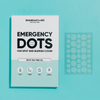 Eine Schachtel Emergency Dots mit Teebaumöl neben einer durchsichtigen Folie mit einzelnen runden Akne-Pflastern.