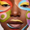 Nahaufnahme eines Gesichts mit bunten, abstrakten Mustern und leuchtend gelbem Augen-Make-up, das mit Danessa Myricks Beauty Colorfix Pastels erstellt wurde.
