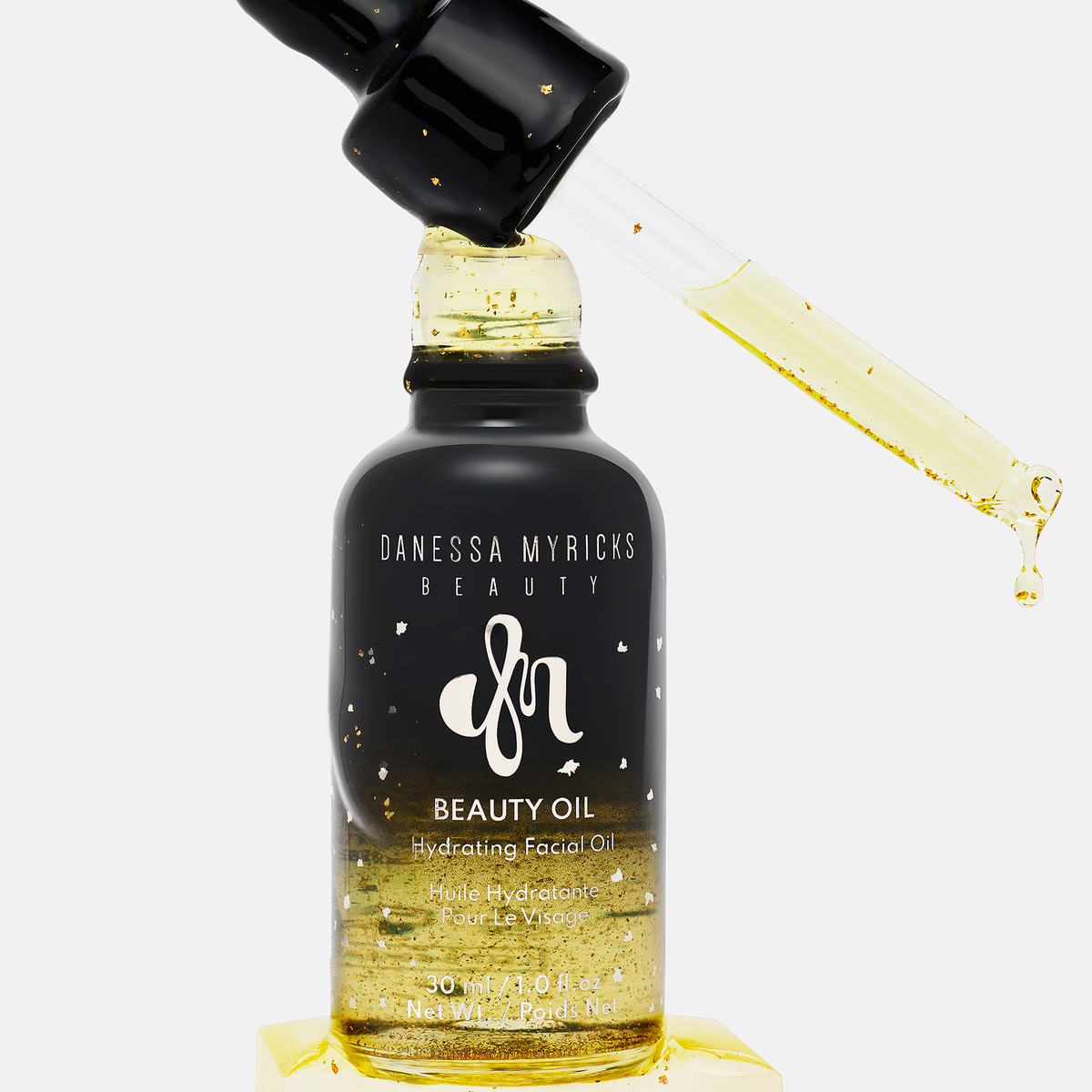 Eine Pipette und ein Fläschchen von Danessa Myricks Beauty Oil Original mit Goldflocken in dem feuchtigkeitsspendenden Gesichtsöl.