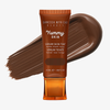 Eine Tube Yummy Skin Serum Tint 15 vor einem tiefbraunem Farbmuster.