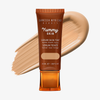 Eine Tube Yummy Skin Serum Tint 4 vor einem mittelbeigem Farbmuster.