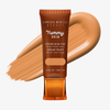 Eine Tube Yummy Skin Serum Tint 8 vor einem warmem dunkelbeigem Farbmuster.