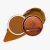 Runde geöffnete bronzefarbene Dose des Yummy Skin Blurring Balm Powder vor einem Farbstreifen der Shade 8.