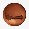 Geschlossener runder bronzener Behälter Yummy Skin Moisture Repair Balm Serum mit Mini-Applikator im Deckel.