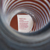 Durch die Windungen einer silbernen Metallfeder ist eine Tube Liquid Rollers Curl Balm sichtbar.