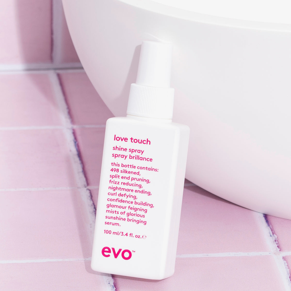 Eine Flasche Love Touch Shine Spray steht auf rosa Fliesen neben einem weißen Waschbecken.