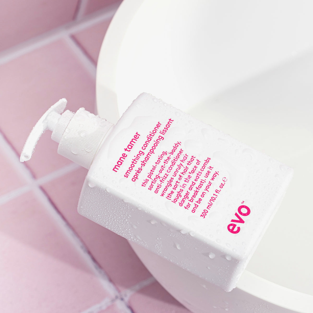 Eine weiße Flasche Mane Tamer Smoothing Conditioner auf einer weißen Wanne neben rosafarbenen Fliesen.