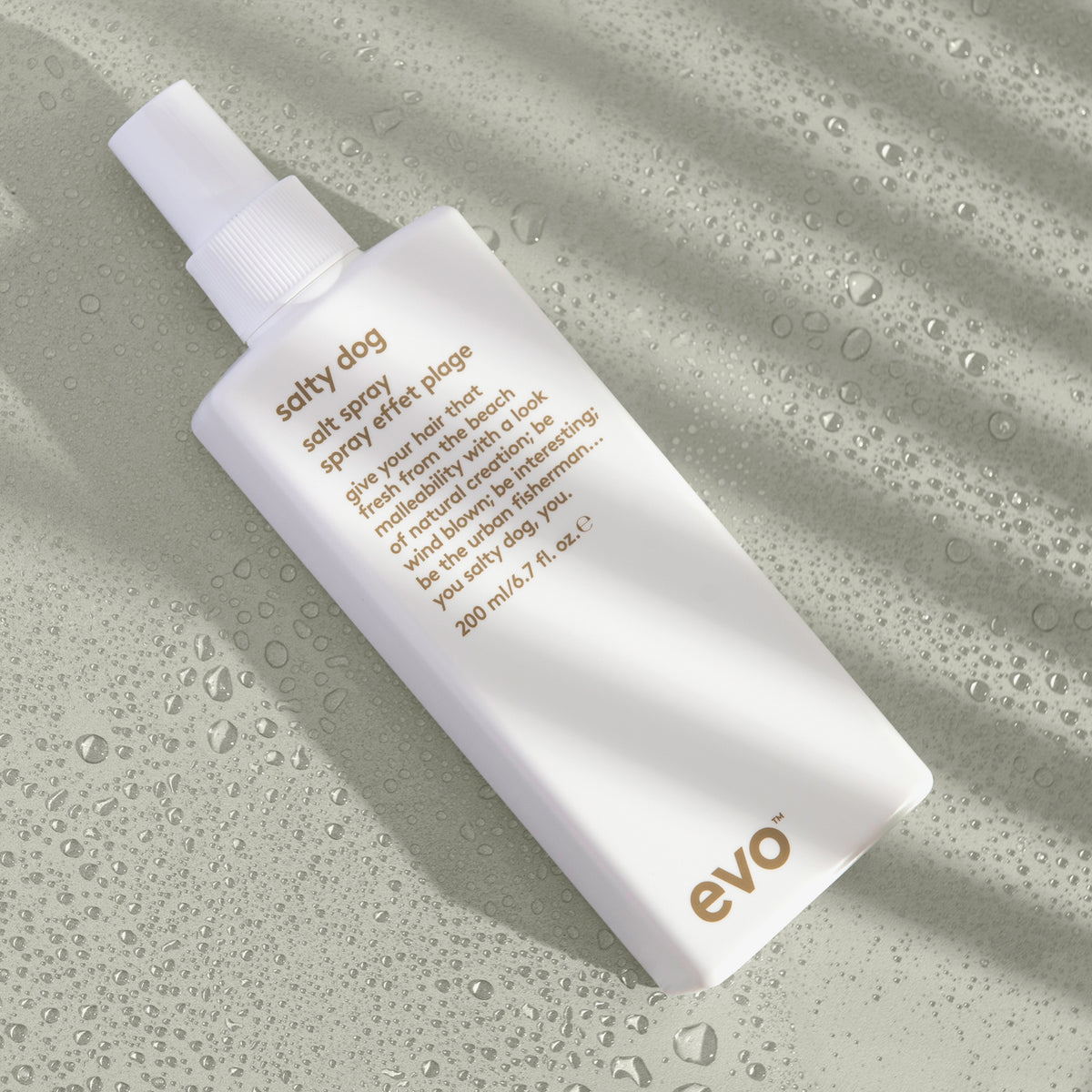 Eine weiße Flasche Salty Dog Salt Spray liegt auf einer nassen salbeigrünen Oberfläche