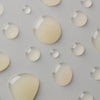 Große und kleine Tropfen des Blemicalm Azelaic Acid 10 % Clarifying Serum auf grauer Oberfläche.