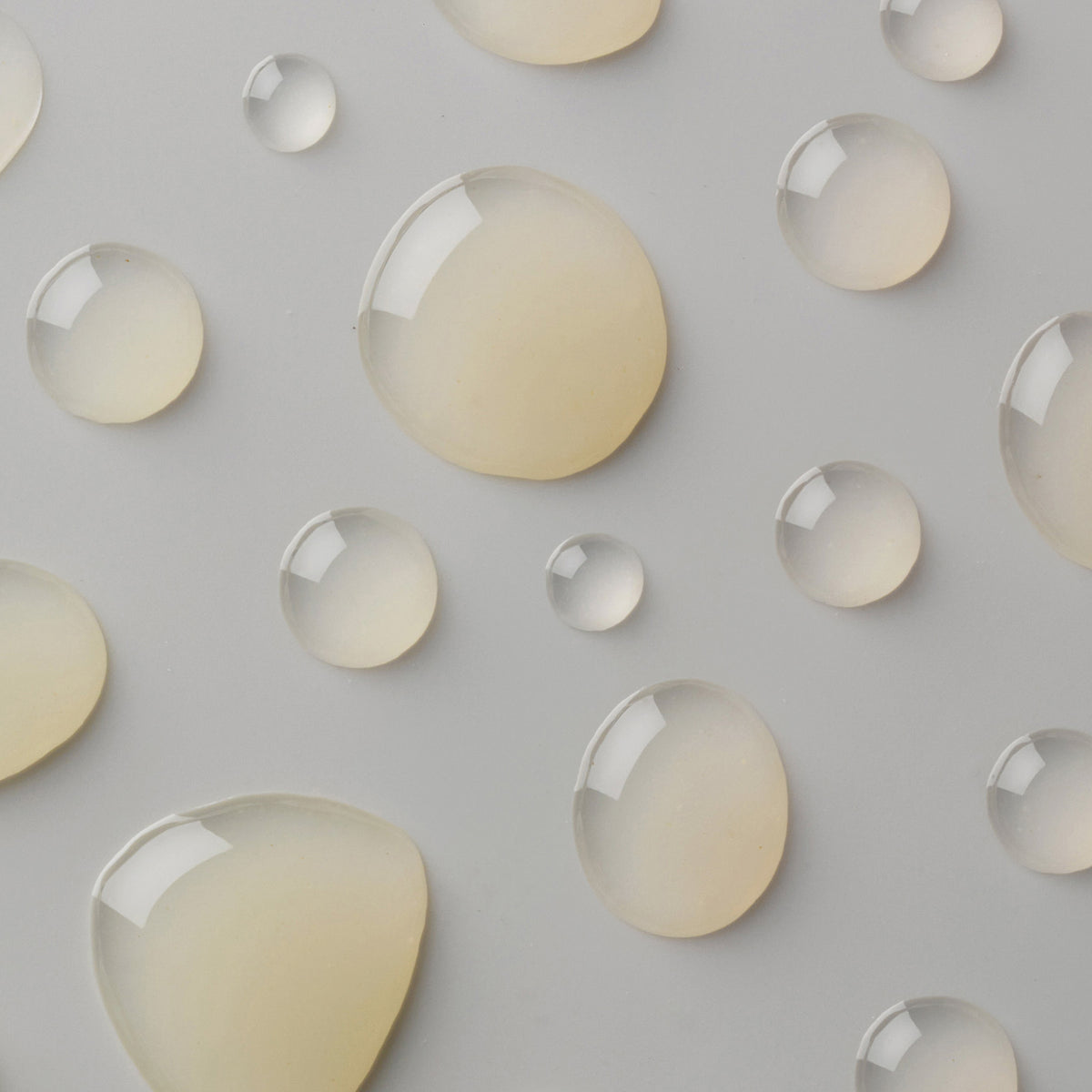 Große und kleine Tropfen des Blemicalm Azelaic Acid 10 % Clarifying Serum auf grauer Oberfläche.