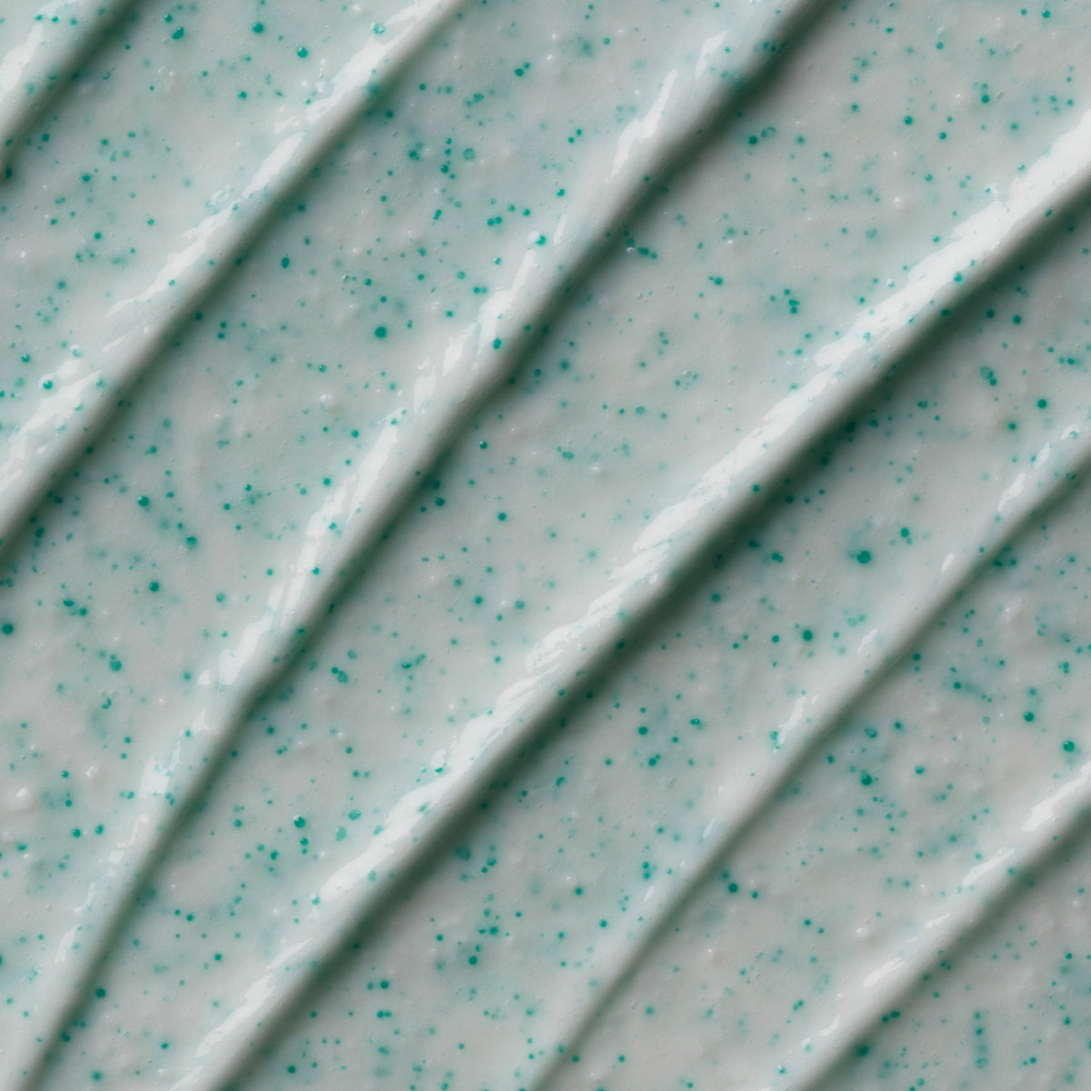 Nahaufnahme der Double Glow Exfoliating Face & Body Scrub, die die blaüliche Textur mit blauen Partikeln zeigt.