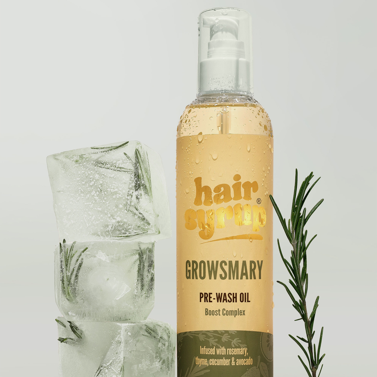 Eine Flasche Hair Syrup Growsmary Pre-Wash Oil wird neben Eiswürfeln und einem Zweig Rosmarin platziert.