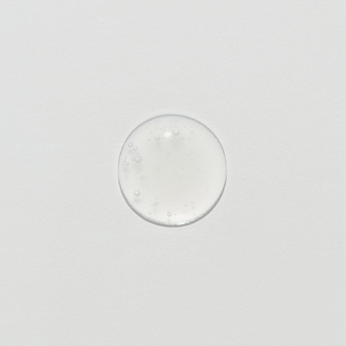 Ein klarer, runder Tropfen Collagen Peptide Hydra Ampoule mit kleinen Bläschen auf einer weißen Oberfläche.