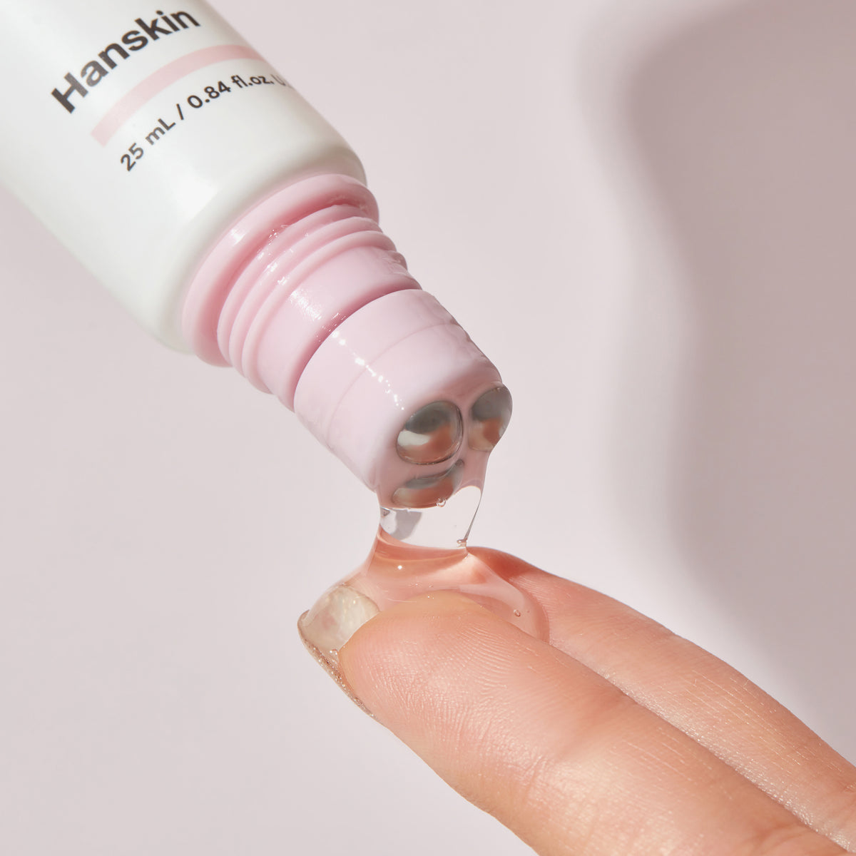 Real Complexion Hyaluron Eye Serum wird vor einem hellen Hintergrund aus einer Hanskin-Flasche auf die Finger einer Person aufgetragen.