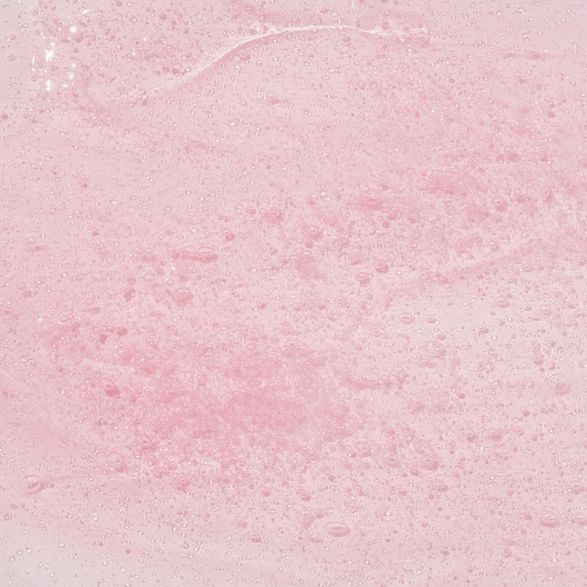 Nahaufnahme der geligen Textur des Real Complexion Hyaluron Pink Capsule Serum auf einer rosa Oberfläche.